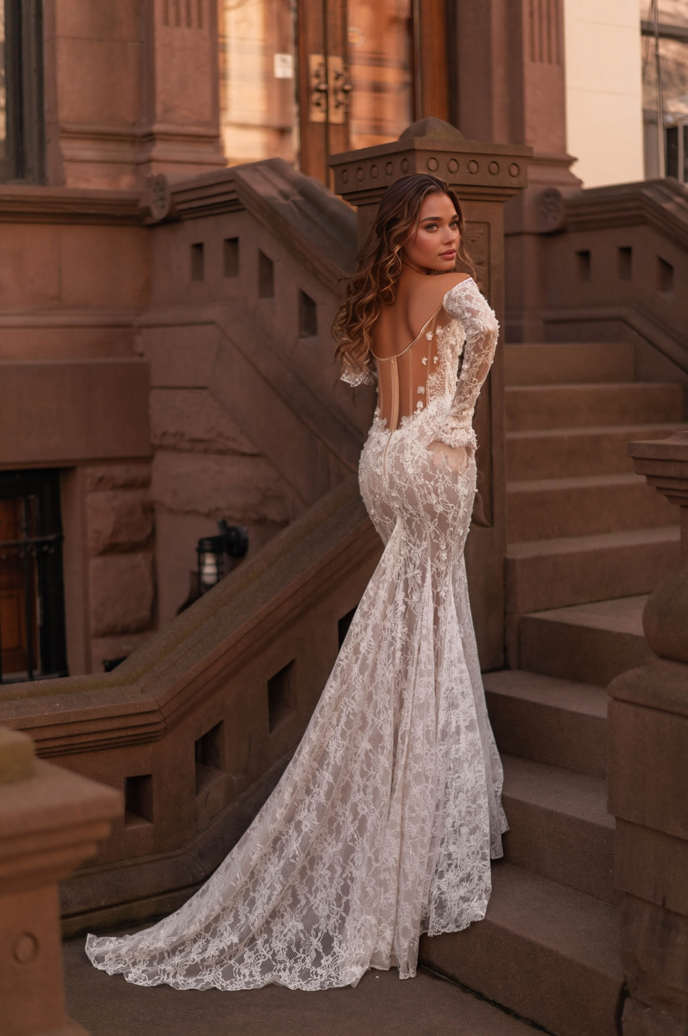 woman wearing a long-sleeve off-shoulder sheer illusion lace wedding dress with cape near a stone building