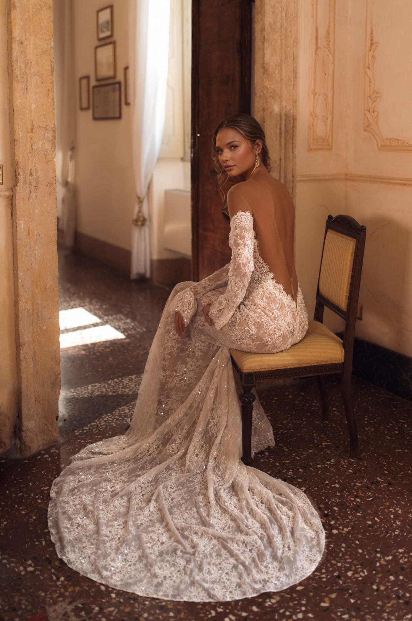 woman in off-shoulder long-sleeve lace wedding dress with open back and long train sitting in a vintage