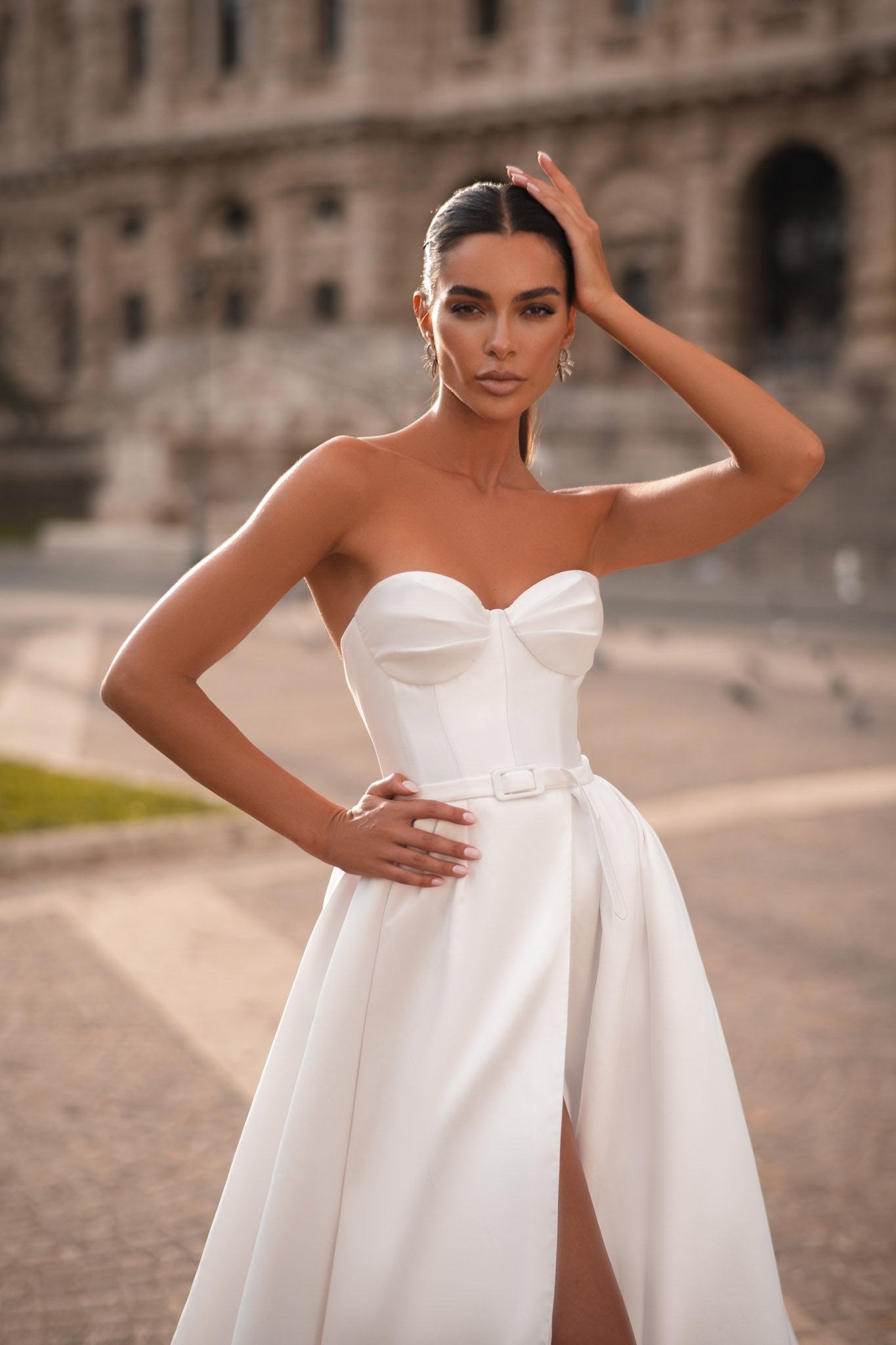 Trendy Modern Off-White Satin Bridal Gown With Sweetheart Neckline, Waist Bow, Sleeveless Design, And Light Flared Train With High Slit