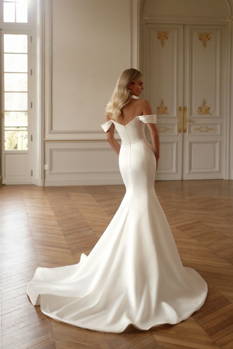 Wedding dress with removable train, beaded pleats, and modern off-shoulder neckline.

