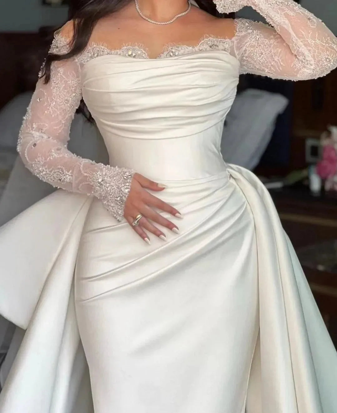 Elegant off-shoulder wedding gown with sheer lace sleeves and draped satin bust design.

