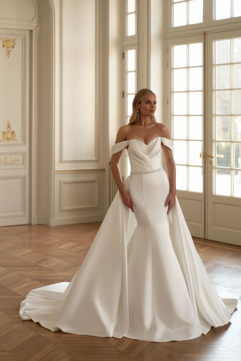 Off-shoulder satin mermaid wedding dress featuring detachable train and beaded pleat details.

