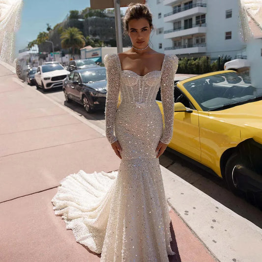 Beaded mermaid wedding dress with illusion sweetheart neckline, long sleeves, and sparkling sequin detail for luxury brides.