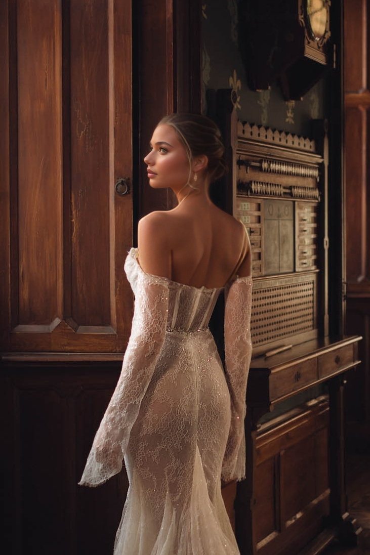 woman wearing a sheer illusion long-sleeve off-shoulder lace wedding dress with long train indoors
