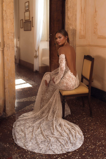 woman in off-shoulder long-sleeve lace wedding dress with open back and long train sitting in a vintage 