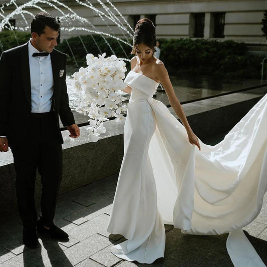Elegant strapless mermaid wedding dress in satin with detachable train, perfect for modern brides.